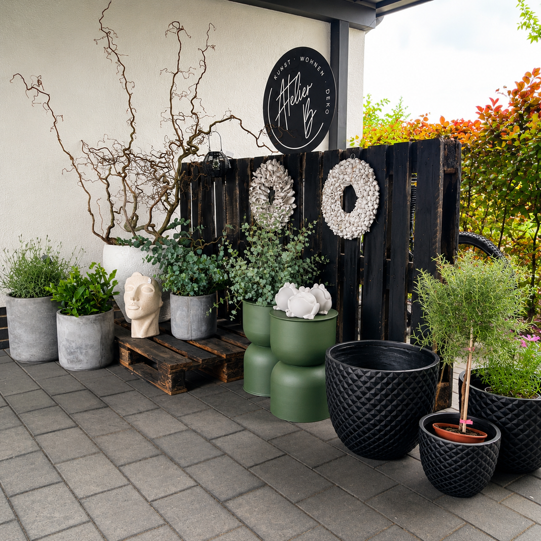 Stilvolle Outdoor-Dekoration von Atelier B mit modernen Pflanzgefäßen, Gartenaccessoires, Kränzen und dekorativen Einzelstücken auf einer überdachten Terrasse im modernen Landhausstil.