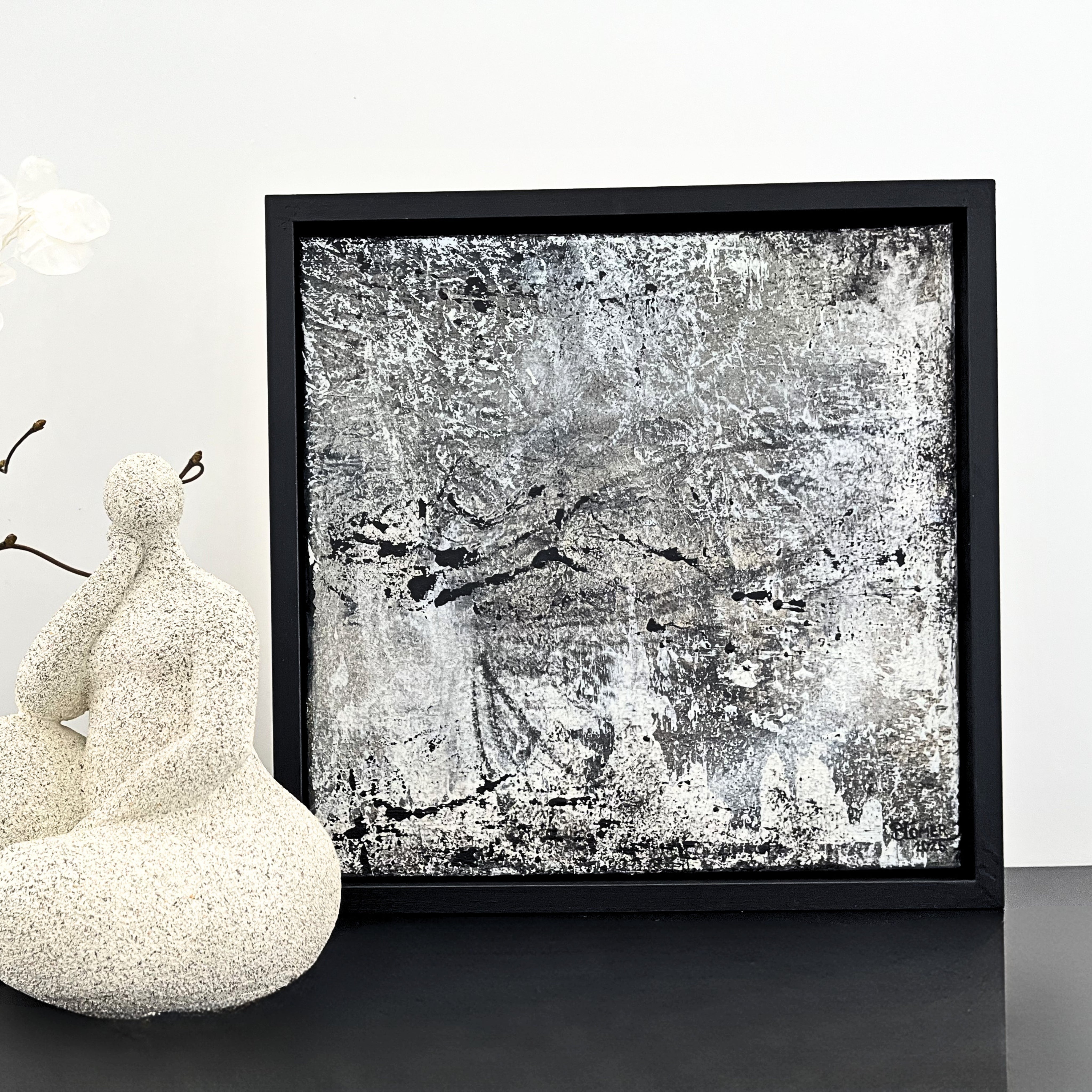 Ein Acrylbild in Schwarz, weiß und grau in einem Schattenfugenrahmen und einer Figur in weiß/sand
