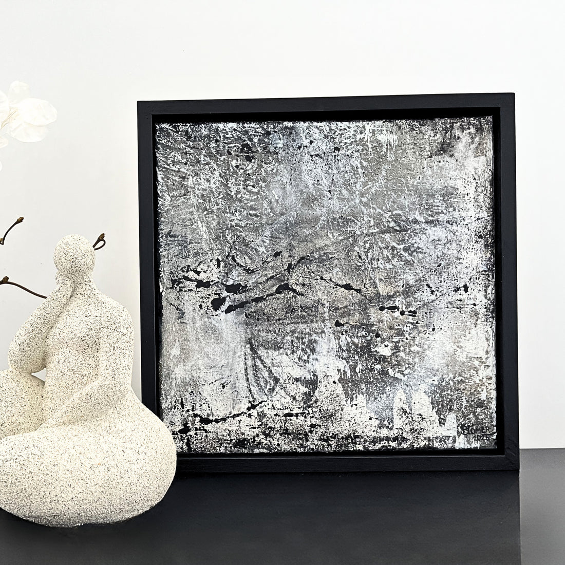 Ein Acrylbild in Schwarz, weiß und grau in einem Schattenfugenrahmen und einer Figur in weiß/sand