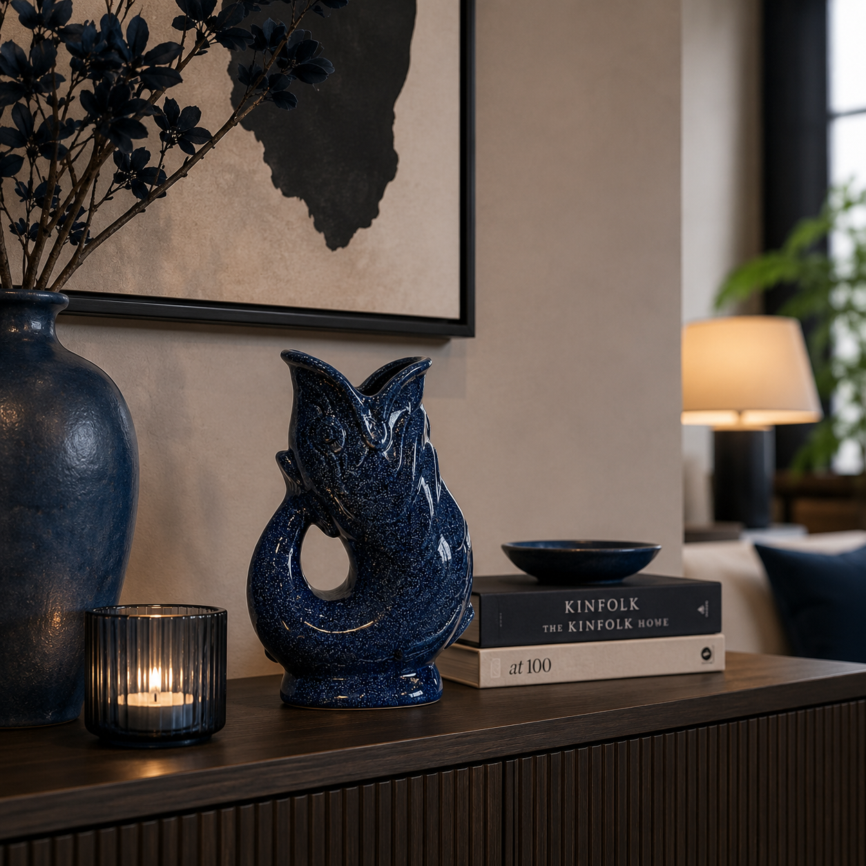 Blaue Fischvase aus Keramik von Atelier B auf einem dunklen Sideboard in einem stilvoll eingerichteten Wohnzimmer. Die dekorative Vase wird von farblich abgestimmter Deko, Kerzenlicht und modernen Wohnaccessoires harmonisch ergänzt.