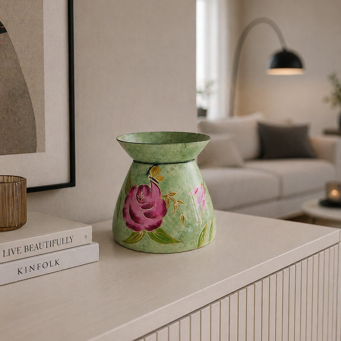 Handbemalte grüne Metallvase mit Blumenmotiv auf einer hellen Kommode in einem modern eingerichteten Wohnzimmer