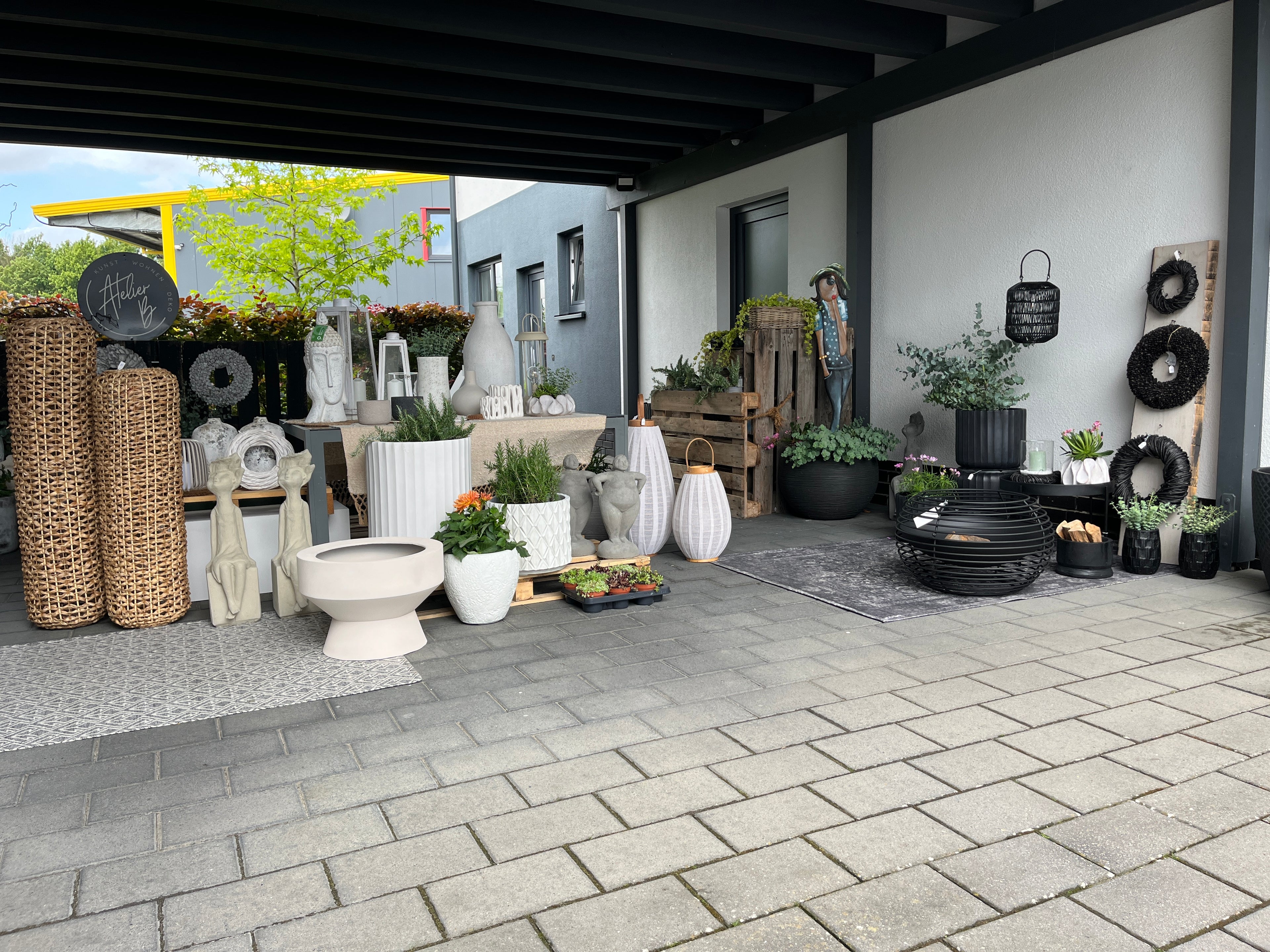 Moderne Outdoor-Living-Dekoration von Atelier B mit stilvollen Pflanzengefäßen, Gartenaccessoires, Laternen und dekorativen Einzelstücken auf einer überdachten Terrasse.