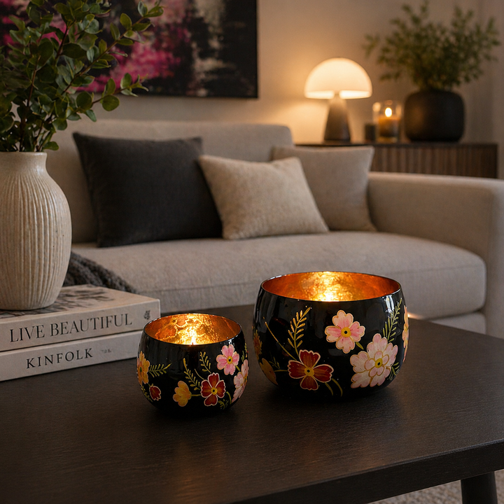 Zwei dekorative Teelichthalter aus Glas in Schwarz und Gold mit Blumenmuster auf einem Wohnzimmertisch im modernen Wohnzimmer mit Kerzenlicht