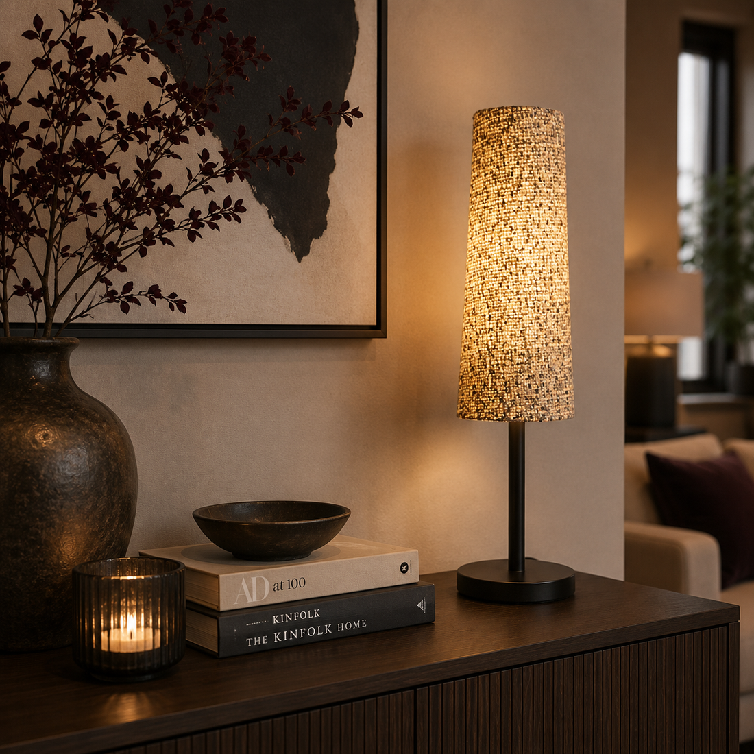 Moderne Tischlampe von Atelier B mit strukturiertem Stoffschirm und warmem Licht auf einem eleganten Sideboard. Die Lampe wird von farblich abgestimmter Dekoration, Kerzenlicht und stilvollen Wohnaccessoires in einem modern eingerichteten Wohnzimmer harmonisch ergänzt.