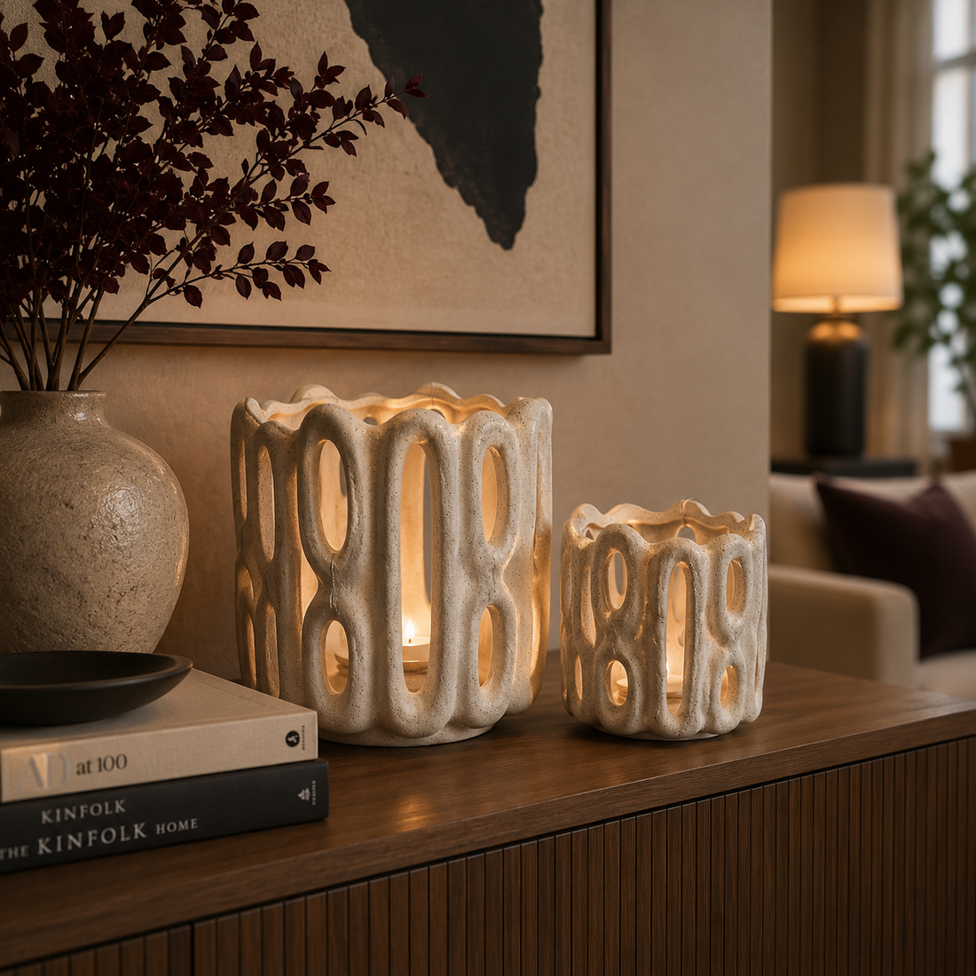 Keramik-Windlicht-Set von Atelier B in zwei Größen auf einem stilvollen Sideboard in modernem Wohnzimmer. Die cremefarbenen Windlichter mit organischer Struktur werden von warmem Kerzenlicht beleuchtet und harmonisch durch Vasen, Bücher und moderne Wohnaccessoires ergänzt.