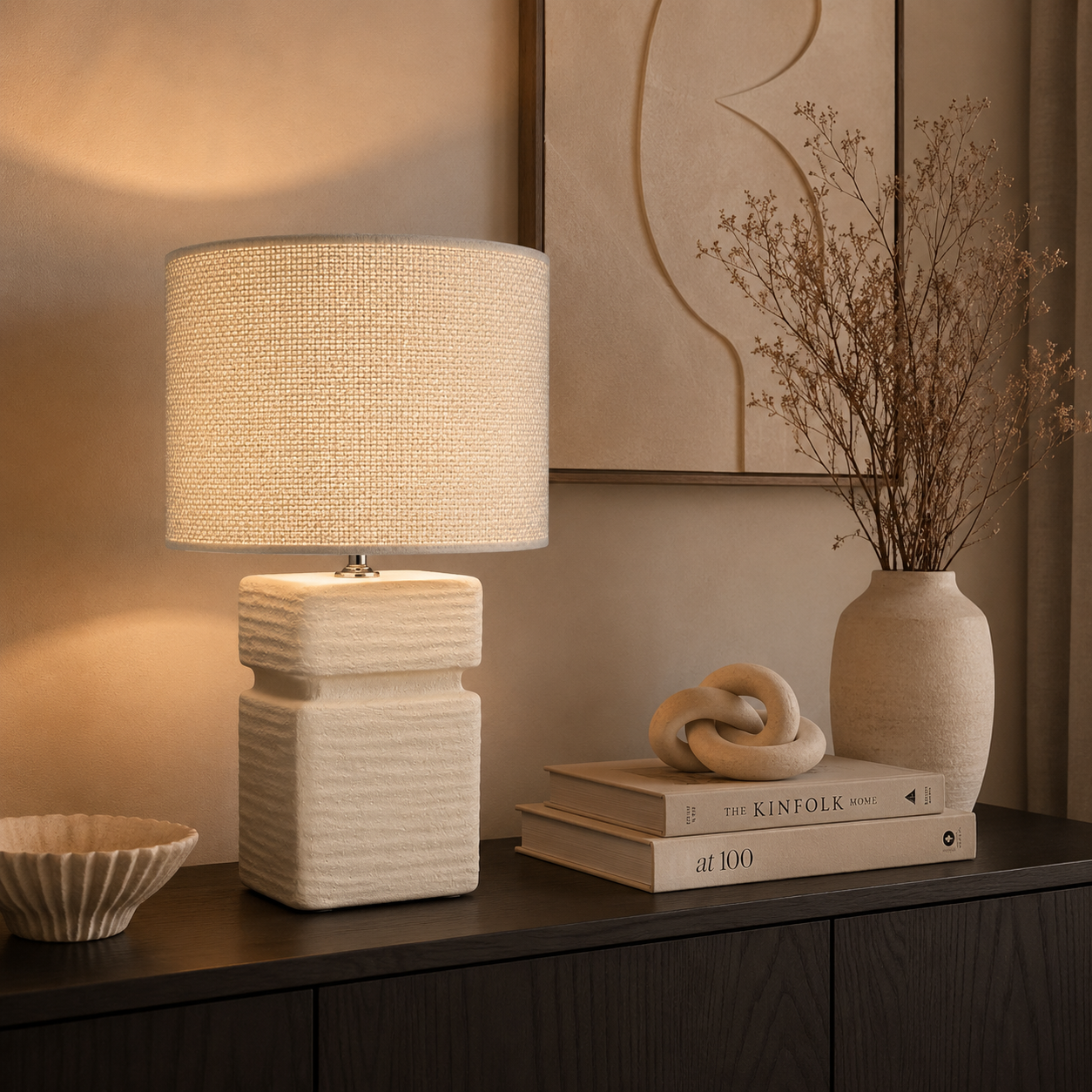 Moderne Keramik Tischlampe von Atelier B mit cremefarbenem Stoffschirm auf dunklem Sideboard in stilvoll eingerichtetem Wohnzimmer mit warmer Beleuchtung und neutraler Dekoration.