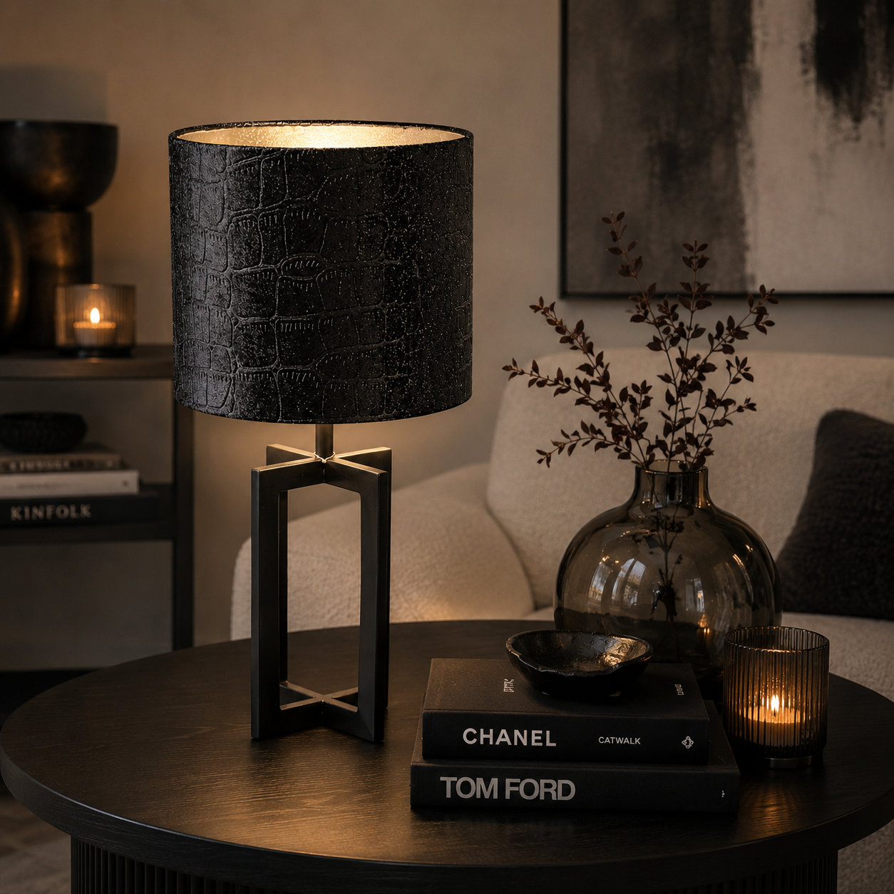Moderne schwarze Tischlampe von Atelier B mit strukturierter Stoffoberfläche und warmem Licht auf einem stilvoll dekorierten Wohnzimmertisch mit dunkler Deko und gemütlicher Atmosphäre.