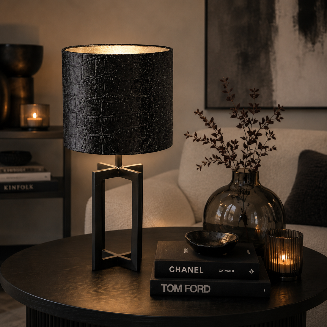 Moderne schwarze Tischlampe von Atelier B mit strukturierter Stoffoberfläche und warmem Licht auf einem stilvoll dekorierten Wohnzimmertisch mit dunkler Deko und gemütlicher Atmosphäre.
