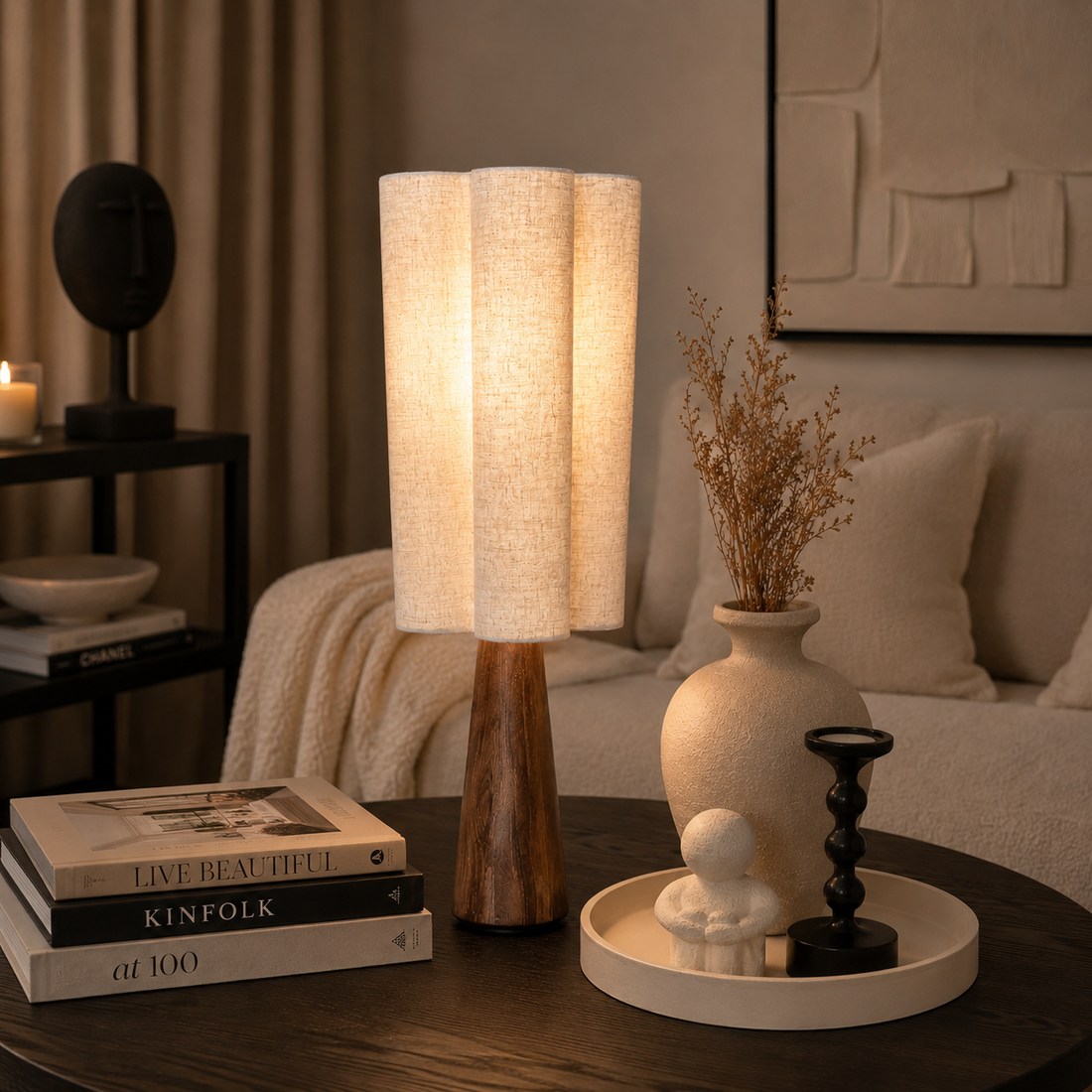 Moderne Tischlampe mit Holzfuß und cremefarbenem Stoffschirm auf einem dunklen Wohnzimmertisch in stilvoll eingerichtetem Wohnzimmer mit warmem Licht und neutraler Dekoration.