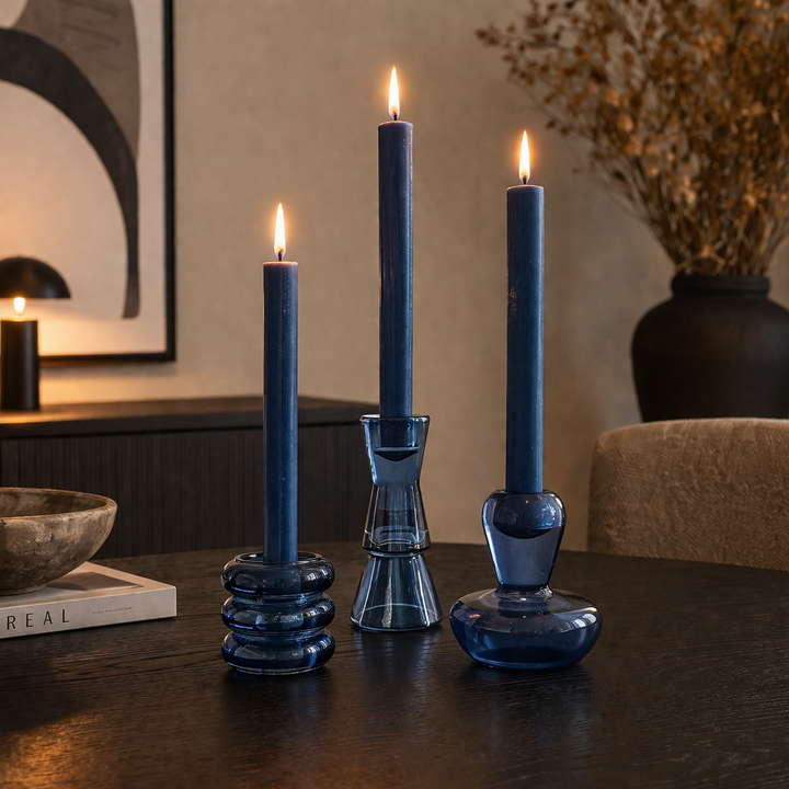 Drei blaue Glas Kerzenständer mit brennenden Kerzen auf einem dunklen Tisch in einem modernen Wohnzimmer mit warmer, gemütlicher Lichtstimmung