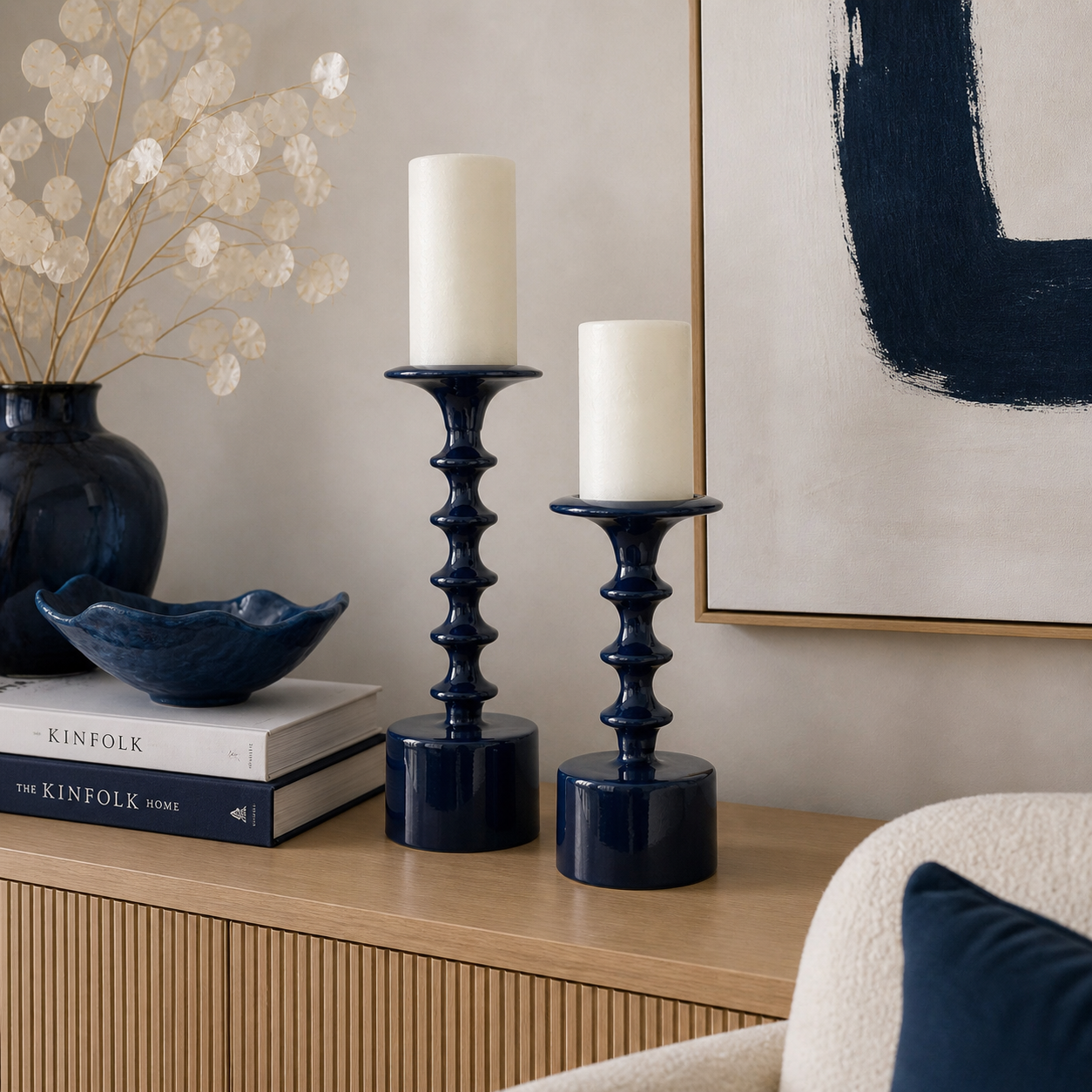 Zwei dunkelblaue Kerzenständer aus Glas mit weißen Stumpenkerzen auf einer Holzkommode in einem stilvoll eingerichteten Wohnzimmer mit blauen Akzenten und moderner Dekoration