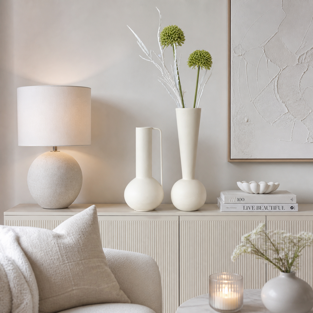 Zwei moderne Metallvasen in creme matt, eine schlank und eine bauchig, dekoriert auf einer Kommode in einem hellen, stilvoll eingerichteten Wohnzimmer mit weißen und cremefarbenen Akzenten