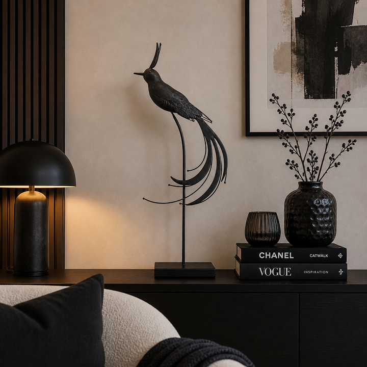 Elegante schwarze Metallvogel-Dekofigur auf einem Ständer, dekoriert auf einer modernen Kommode in einem stilvoll eingerichteten Wohnzimmer mit schwarzen Akzenten und warmer Beleuchtung.