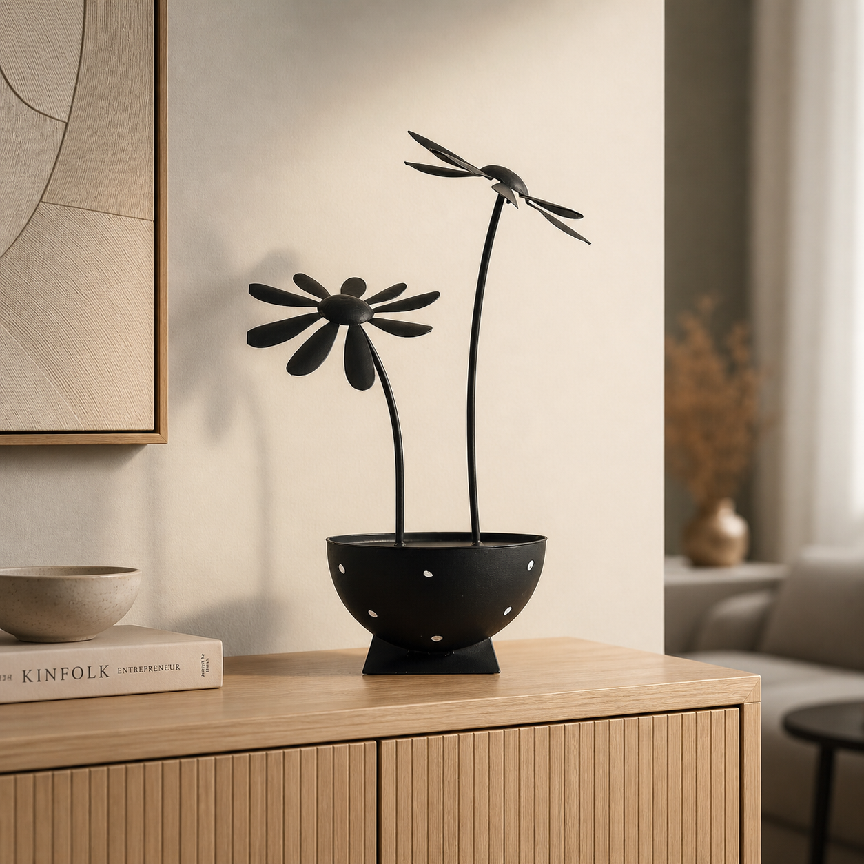 Schwarze Metallblumen Skulptur auf einem hellen Holz Sideboard in einem minimalistischen Wohnzimmer mit weichem, warmem Licht und stilvoller Dekoration